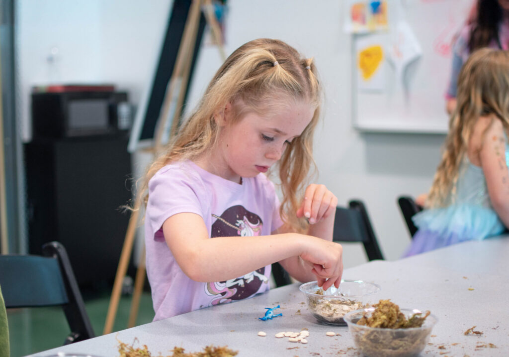 A young girl participates in a hands-on learning activity at Discovery Gateway Children’s Museum in Salt Lake City, exploring art and science through creative play with natural materials like moss and seeds.